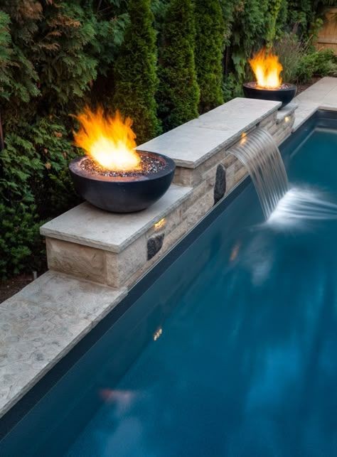Spillover waterfall water features and fire bowls sit on custom masonry poolside